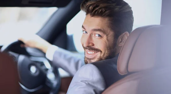 Egy jóképű, mosolygós üzletember portréja, aki a kocsiját vezeti. — Stock Fotó
