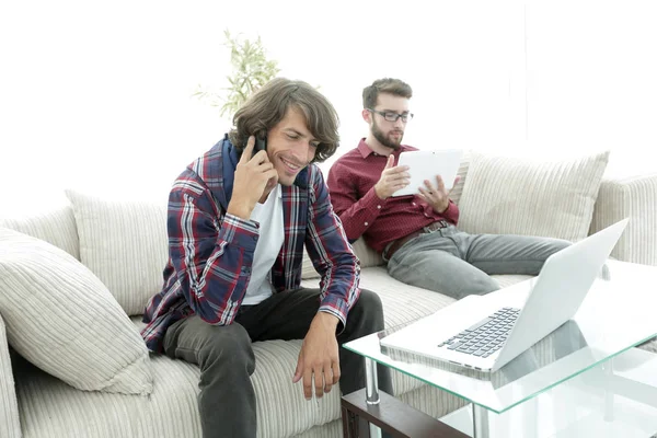 Δύο τύποι κάθονται στον καναπέ, μιλάμε για ένα κινητό τηλέφωνο και κουβέντα στο διαδίκτυο. — Φωτογραφία Αρχείου