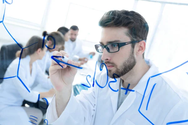 De derrière le verre.scientist écrit un marqueur sur un panneau de verre . — Photo