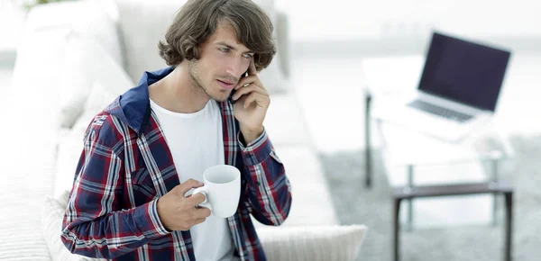 Beautiful guy with a cup sits in front of a laptop. — Stock Photo, Image