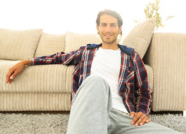 Kendine güvenen adam rahat bir oturma odasında halı üzerinde oturan.