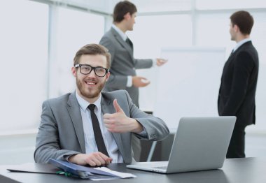 Yönetmen açık bir dizüstü bilgisayar ve kağıtları ile masada oturuyor.