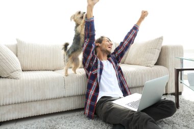 Mutlu adam oturma odasındaki kanepenin yanında köpeğiyle seviniyor..