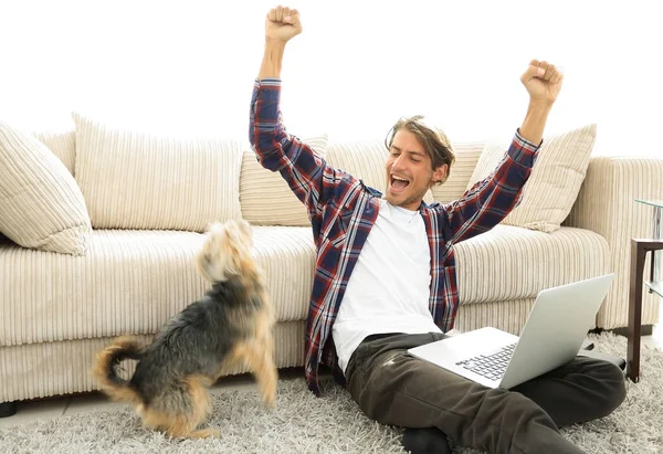 Jovem feliz exulta com seu cão sentado na sala de estar — Fotografia de Stock