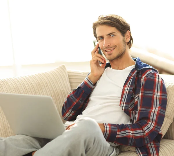 Serious young man with laptop talking on mobile phone — Stock Photo, Image