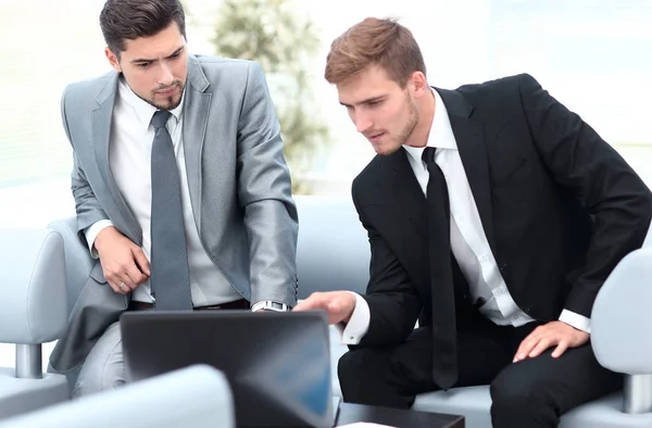 Dois colegas trabalhando em um laptop sentado no lobby do escritório . — Fotografia de Stock