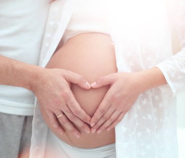 Onun bebek bu üzerinde bir kalp şeklinde ellerini tutan hamile kadın