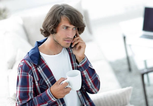 Hermoso chico con una taza se sienta delante de un ordenador portátil . — Foto de Stock