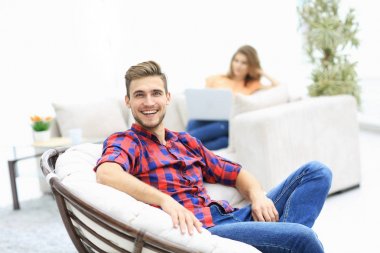 Bulanık arka planda büyük bir sandalyede oturan mutlu genç adam.