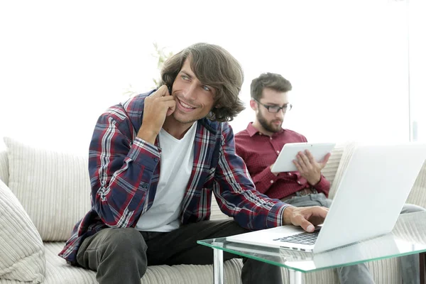 Dwóch facetów siedzi na kanapie, rozmawiając na smartfonie i komunikowania się przez Internet. — Zdjęcie stockowe