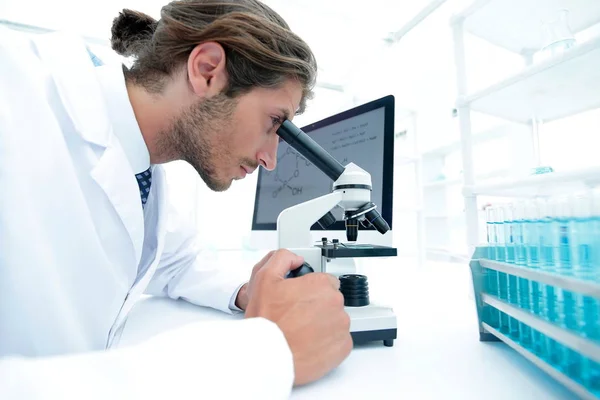 Young laboratory scientist looking at microscope in laboratory — Stock Photo, Image