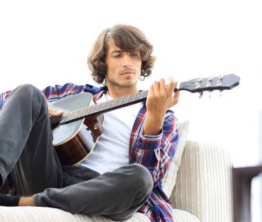 Yakışıklı adam evde kanepede gitar çalmaya