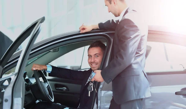 Joven hombre elegir el coche en el salón con la ayuda de un consultor — Foto de Stock