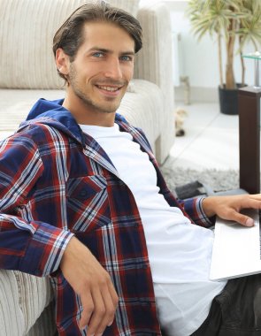 kanepede yakın katta oturan dizüstü bilgisayar ile gülümseyen genç adam