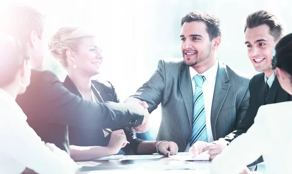 Geschäftskollegen sitzen an einem Tisch während eines Meetings mit zwei männlichen Führungskräften beim Händeschütteln — Stockfoto