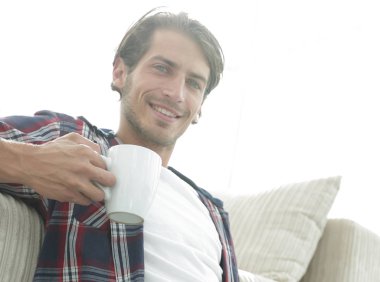 genç adam kanepede yakın katta oturan bir fincan tutan dizüstü bilgisayar ile