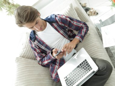 dizüstü bilgisayar ve akıllı telefon oturma odasında ciddi genç adam.