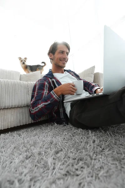 Jongeman is het drinken van thee zittend op de vloer in de buurt van de Bank. — Stockfoto