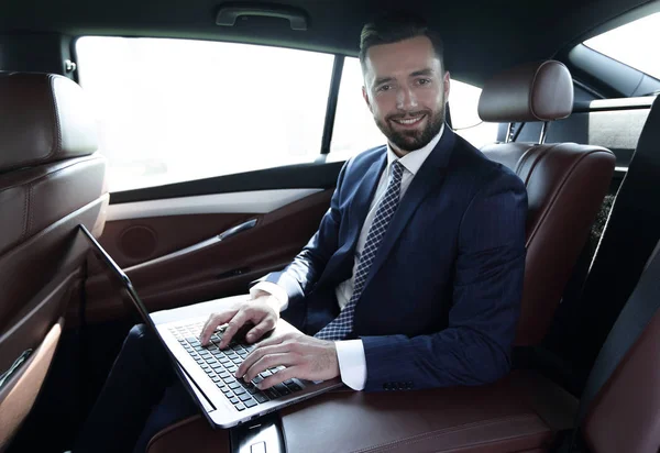 坐在车里的笔记本电脑键盘上工作的商人 — 图库照片