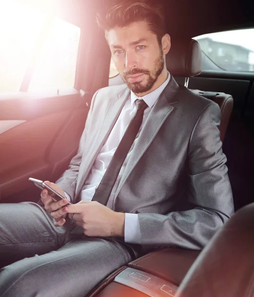 快乐年轻的商人，在汽车的后座中使用手机 — 图库照片