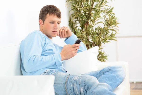 Bilden av en ung man sitter i soffan och med en telefon — Stockfoto