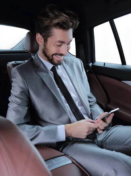 Muž v obleku, sedí v autě a čtení zpráv na smartphone — Stock fotografie