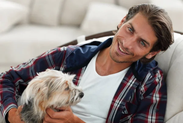 Schöner Kerl streichelt seinen Hund, während er in einem großen Sessel sitzt. — Stockfoto