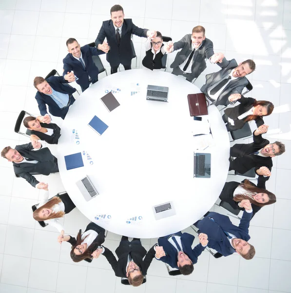 Directeur en business team zitten aan de ronde tafel en houden elkaars handen vast. — Stockfoto