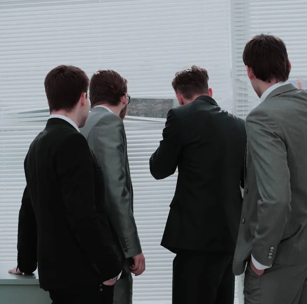 Επιχειρηματική ομάδα πιέζει τα blinds και κοιτάζοντας έξω τον άνεμο γραφείο — Φωτογραφία Αρχείου
