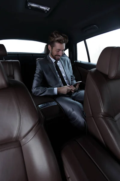 Man in suit sitting in car and reading messages on smartphone — Stock Photo, Image