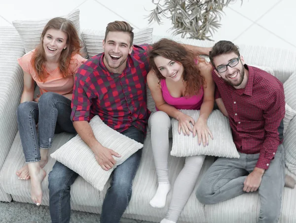 Alegre grupo de amigos ríen, sentado en el sofá . — Foto de Stock