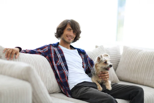 Snygg kille sitter i soffan med sin hund. — Stockfoto