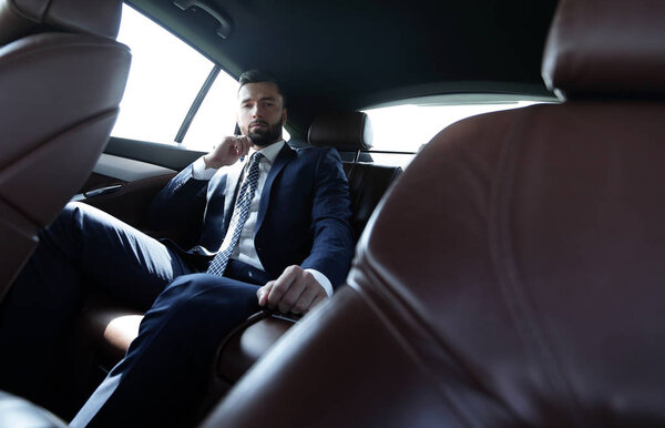 businessman talking on the phone while sitting in the back seat of his car