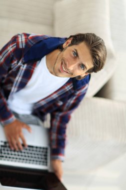 dizüstü bilgisayarda çalışan ve kameraya bakarak bir genç adam. Yukarıdan görüntülemek