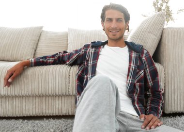 Kendine güvenen adam rahat bir oturma odasında halı üzerinde oturan.