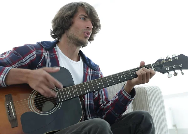 Cara canta uma música e toca guitarra sentado no sofá . — Fotografia de Stock