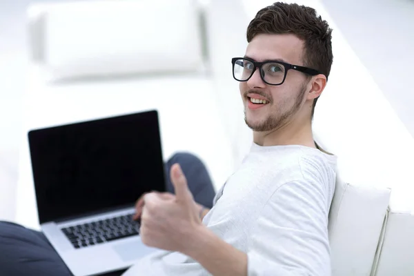 Moderno joven sentado delante de la computadora portátil abierta y mostrando el pulgar hacia arriba —  Fotos de Stock