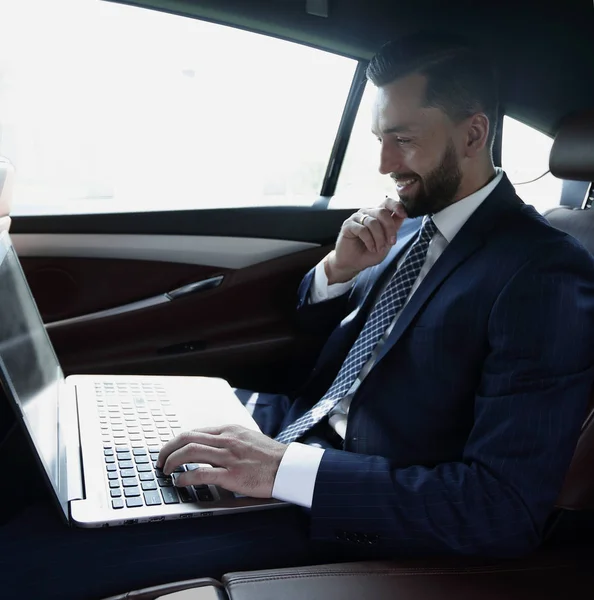 Empresario escribiendo texto en el ordenador portátil mientras está sentado en el coche —  Fotos de Stock