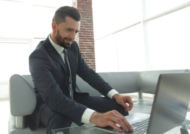 ofis lobisinde otururken dizüstü bilgisayar üzerinde çalışan iş adamı