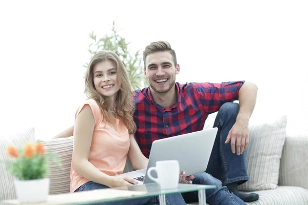 Young couple of students uses a laptop sitting on sofa — Stock Photo, Image