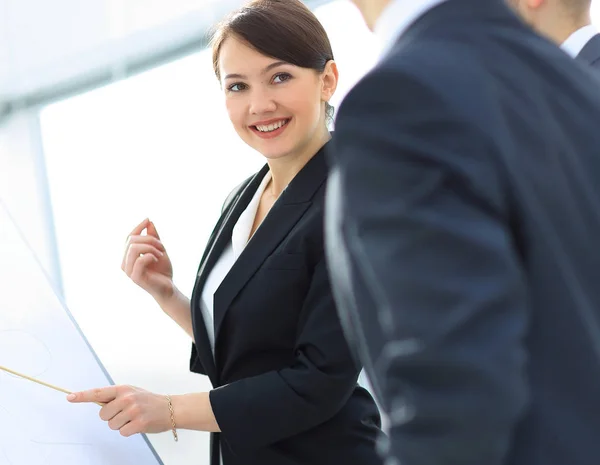 Lächelnde Geschäftsfrau zeigt Kollegen Informationen auf dem Flipchart. — Stockfoto