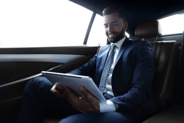 bir arabanın arka koltuğunda çalışma ve bir tablet kullanarak iş adamı