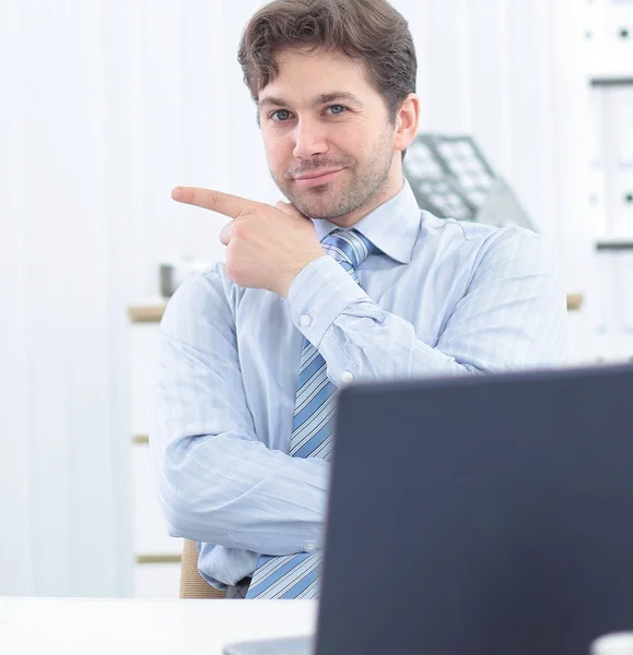 Belo homem de negócios sentado atrás de uma mesa e apontando para espaço de cópia — Fotografia de Stock