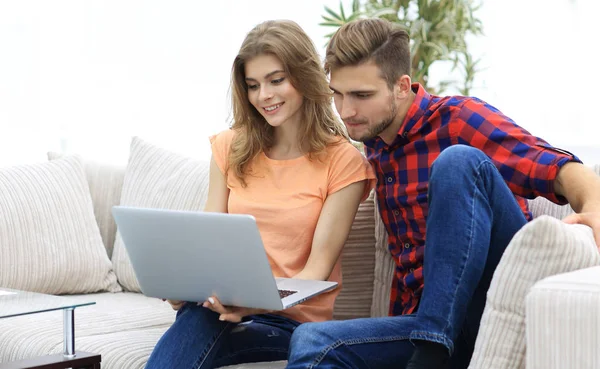 Молодий чоловік зі своєю дівчиною дивиться на ноутбук, що сидить на дивані . — стокове фото