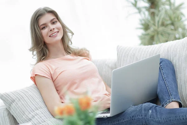 Gyönyörű lány, egy laptop, ül a kanapén. — Stock Fotó