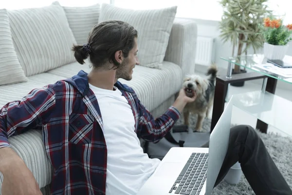 Elegante giovane uomo accarezzando il suo animale domestico e lavorando sul computer portatile — Foto Stock