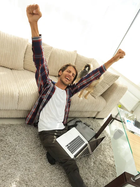 Ευτυχισμένος ο τύπος με το laptop περιχαρής στο ευρύχωρο σαλόνι. — Φωτογραφία Αρχείου
