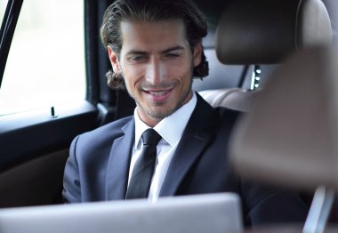 Adam arabada otururken dizüstü bilgisayarla çalışıyor.