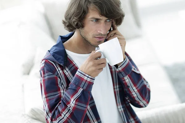 Hermoso chico con una taza se sienta delante de un ordenador portátil . — Foto de Stock