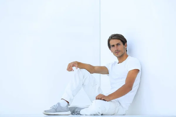 Сумний молодий чоловік сидить біля білої стіни — стокове фото
